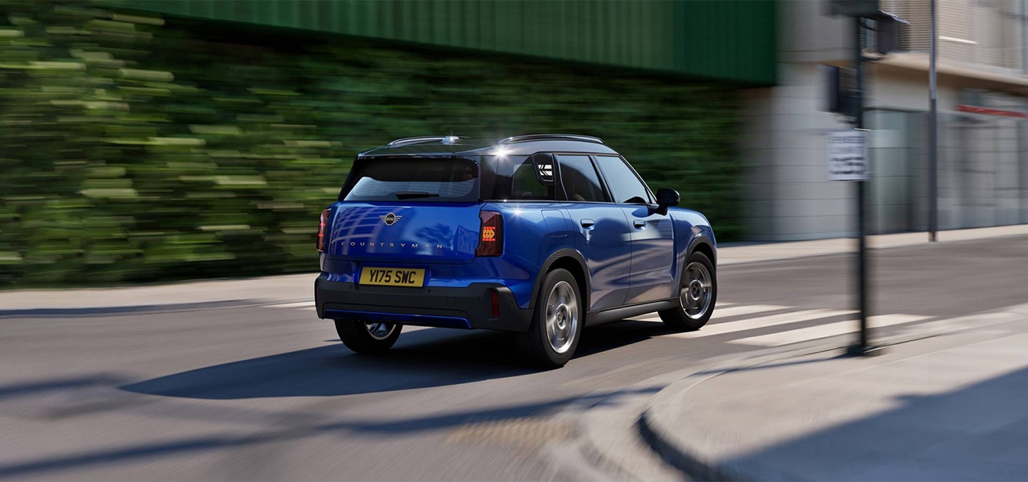 Side rear view of the MINI Countryman in Nanuq White with Black Roof standing on a street.